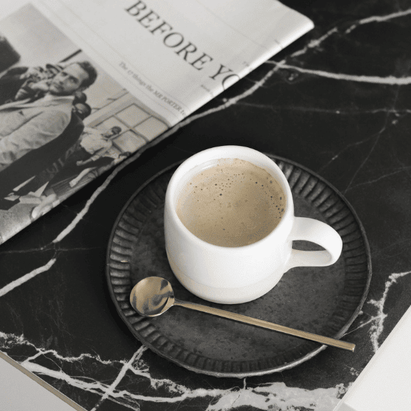 White Cup of Coffee on a black plate with a french magazine.