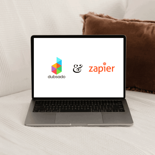 Laptop showing the Dubsado and Zapier logos. The laptop is on a white sofa with a brown cushion.