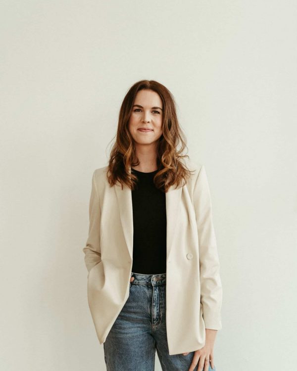 Brand & Website designer standing against a beige wall with a hand in her pocket.