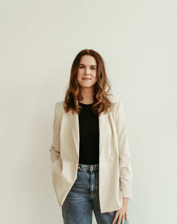 Brand & Website designer standing against a beige wall with a hand in her pocket.